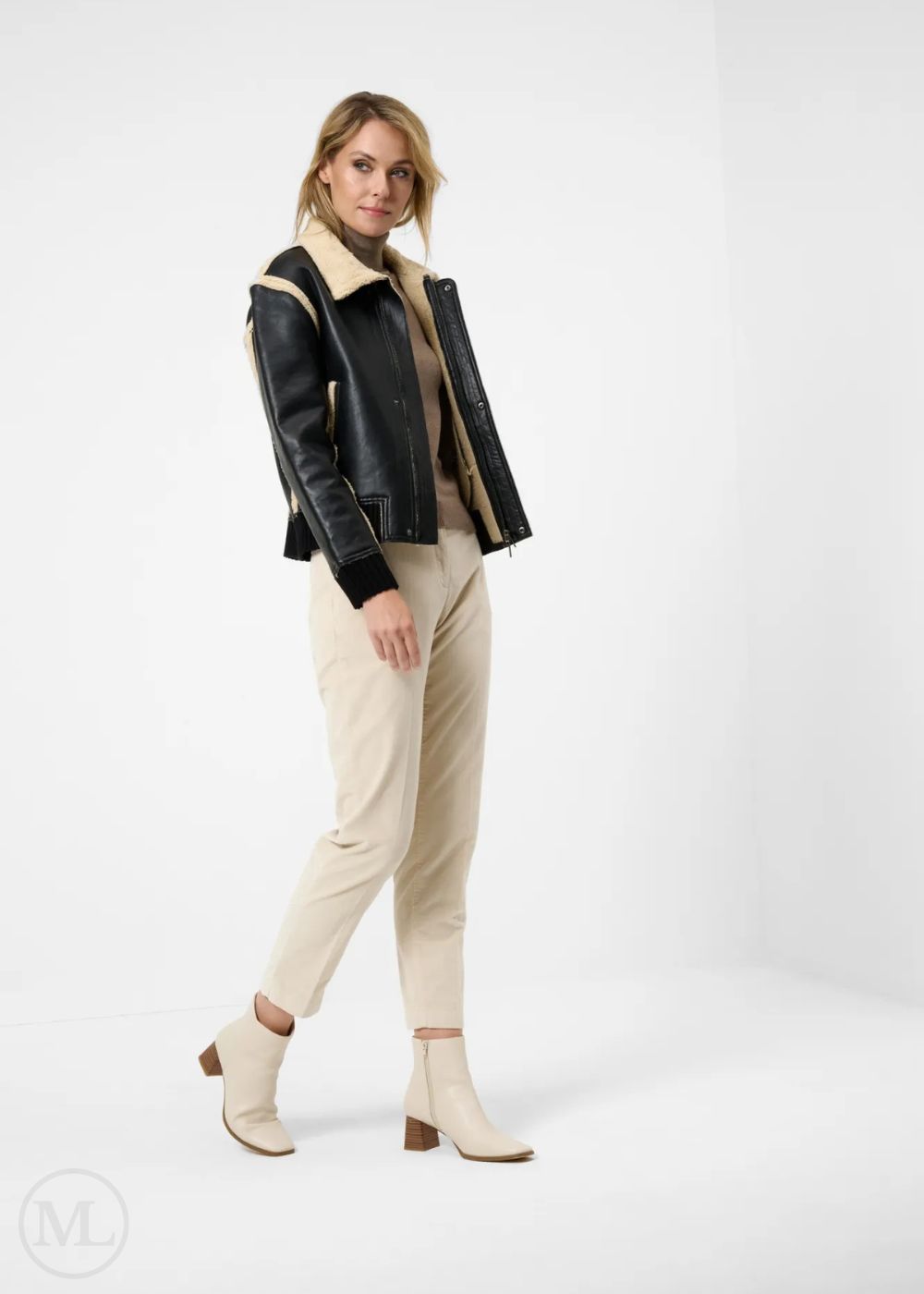 Woman wearing a black leather aviator jacket with shearling collar, beige sweater, pants, and boots on a white background